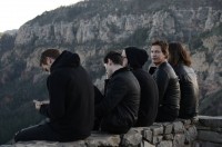an image of the band sitting on a ledge from behind. The lead singer is the only one turned around looking at the camera.