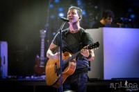 lead singer playing an acoustic guitar on stage and singing.