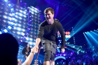 lead singer shaking a crowd members hand on stage.